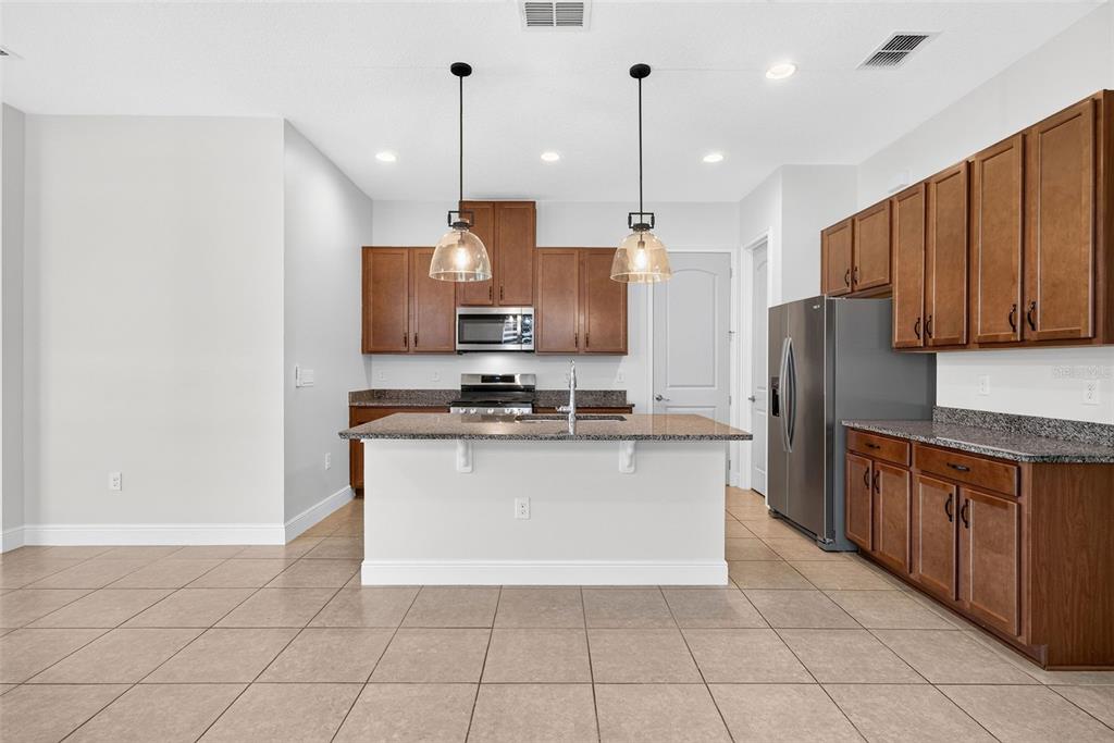 A kitchen features brown wooden cabinets, granite countertops, a central island, and stainless steel appliances — 2286 DATURA LOOP, ST CLOUD, FL