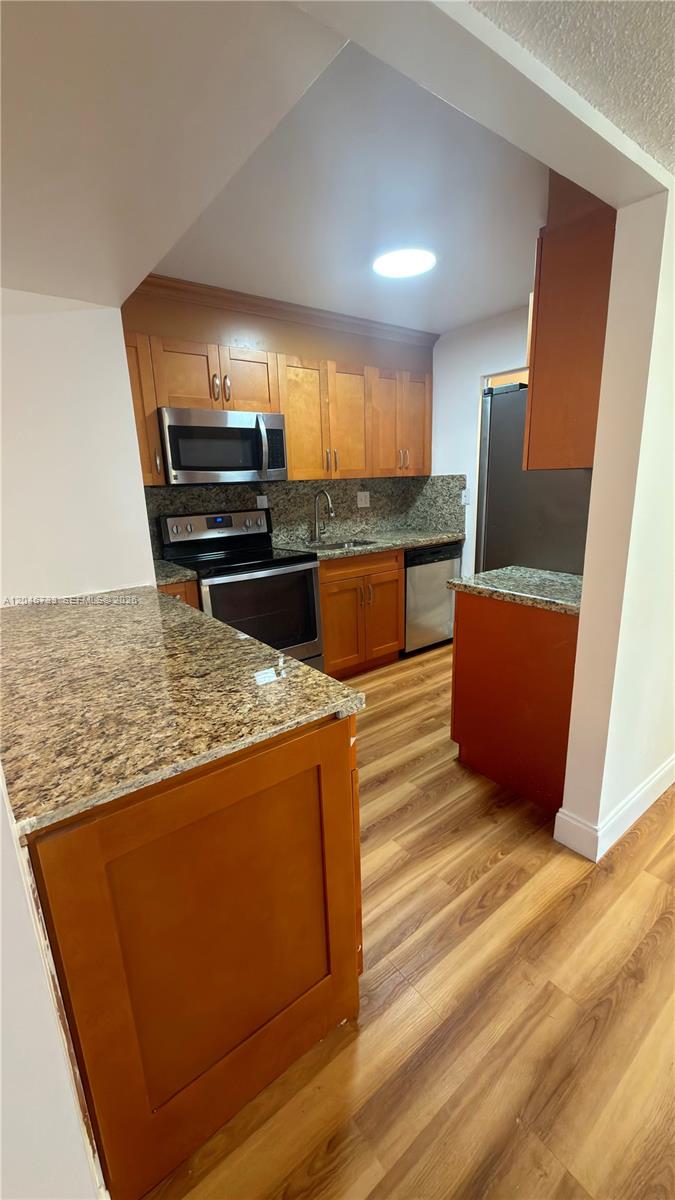 A kitchen features wood cabinets, granite countertops, stainless steel appliances, and wood-look flooring — 469 NE 207th Ln # 101, Miami FL 33179, MIAMI, FL