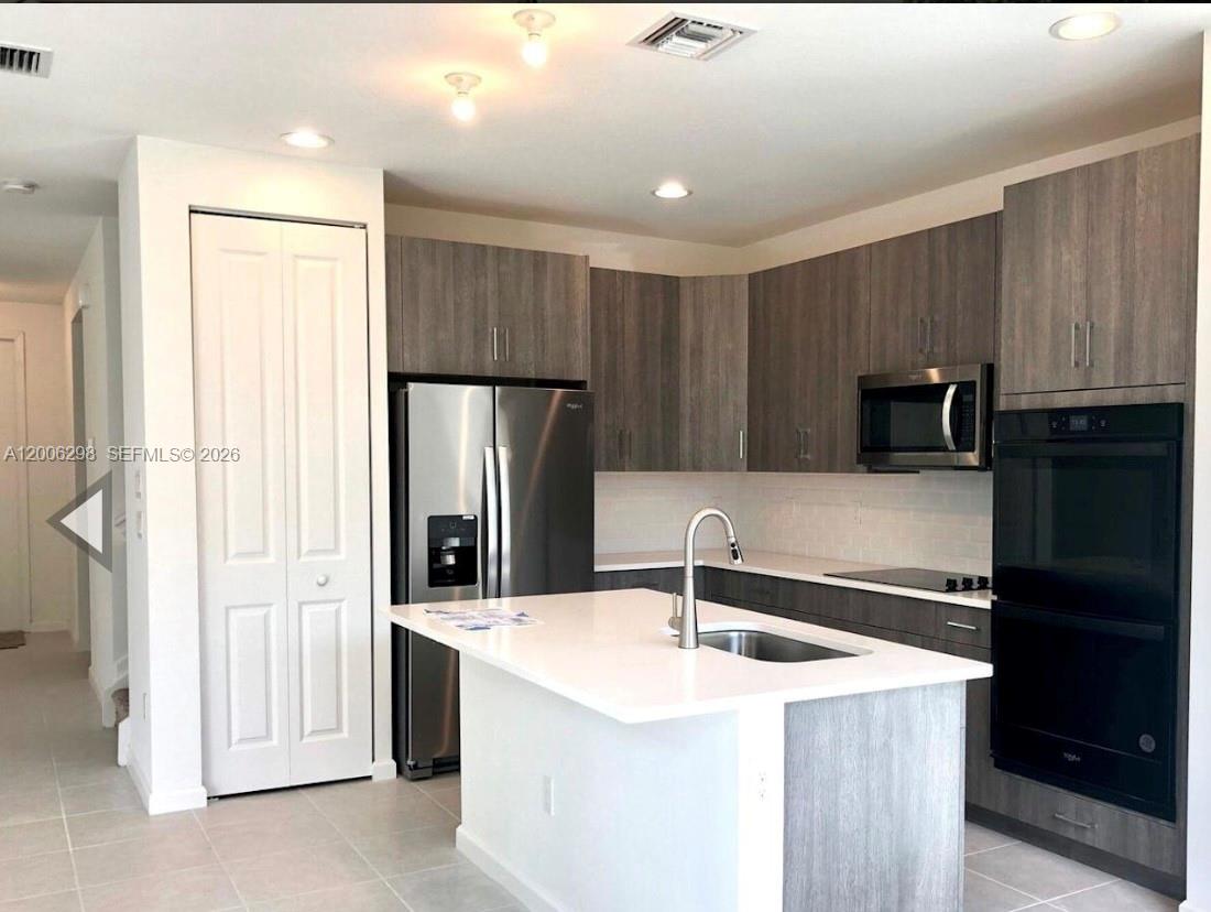 A modern kitchen features gray wood-grain cabinets, stainless steel appliances, and a white quartz island — 3525 NW 1st St, Pompano Beach FL 33069, POMPANO BEACH, FL