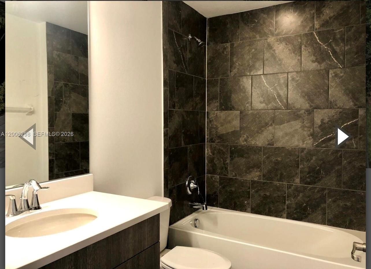 A bathroom features a white vanity, a mirror, and a bathtub with dark tiled walls — 3525 NW 1st St, Pompano Beach FL 33069, POMPANO BEACH, FL
