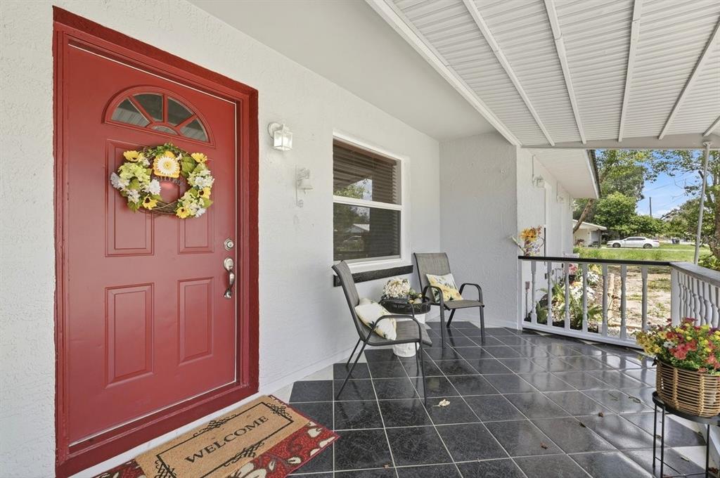 A covered front porch features black tile flooring, a red front door, and outdoor seating — 3126 MARLIN DRIVE, SEBRING, FL