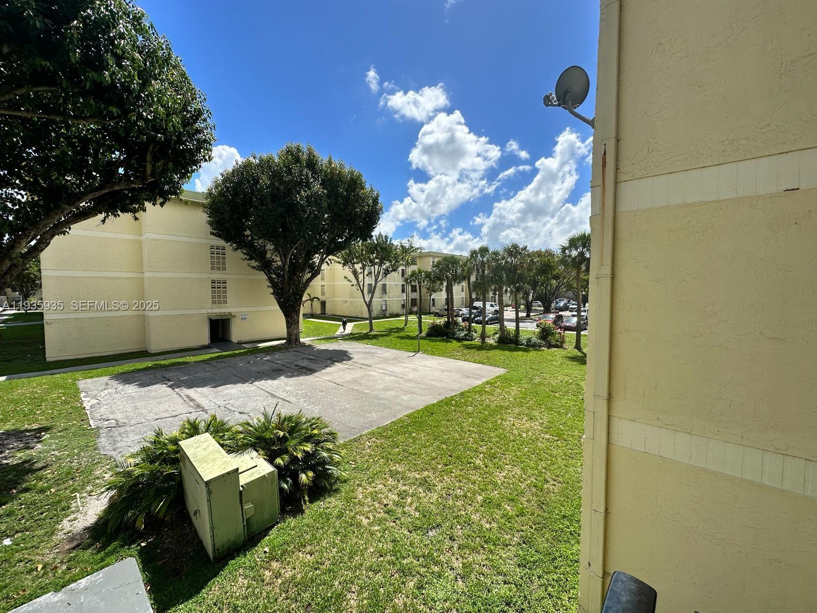 An exterior view shows a paved courtyard between multi-story apartment buildings with surrounding green lawns — 1875 W 56th St # 301, Hialeah FL 33012, HIALEAH, FL