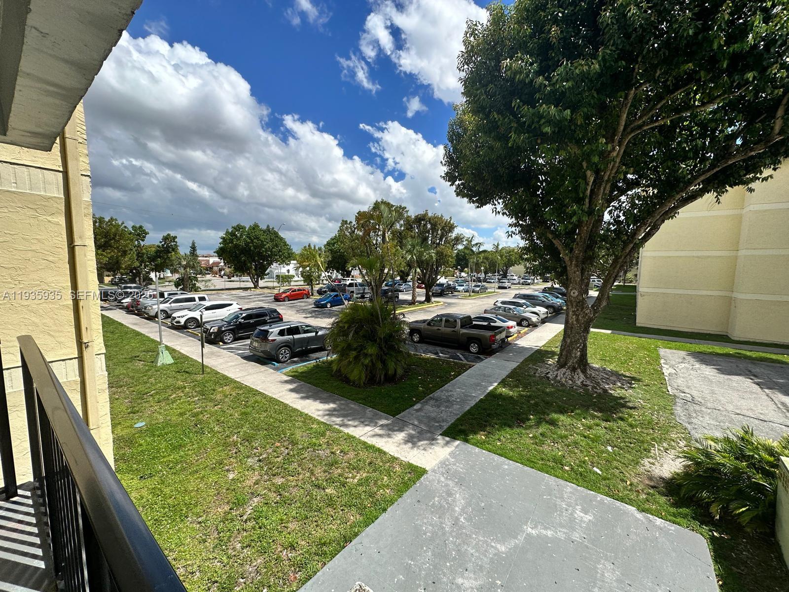 An elevated view of a parking lot surrounded by grass, trees, and apartment buildings — 1875 W 56th St # 301, Hialeah FL 33012, HIALEAH, FL