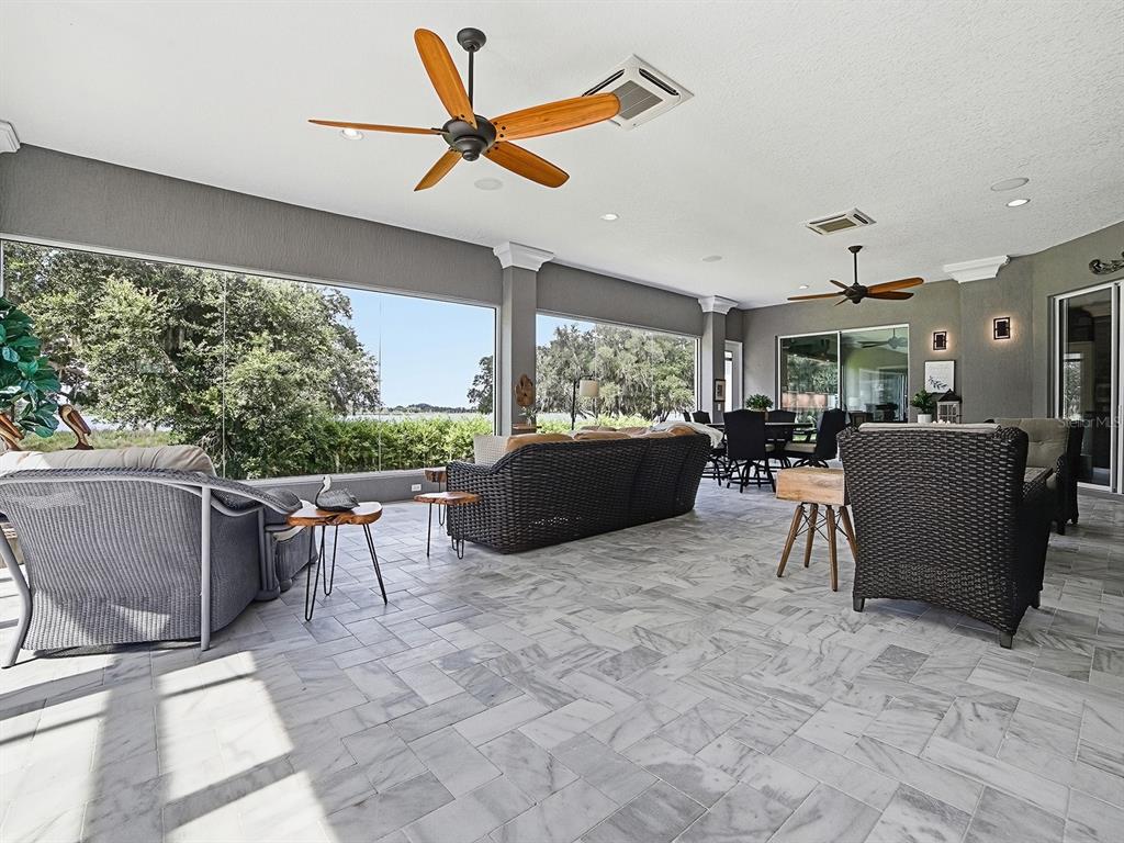 A spacious covered patio features marble tile flooring, wicker furniture, and large glass wall panels — 1792 LAKE MIONA DRIVE, THE VILLAGES, FL