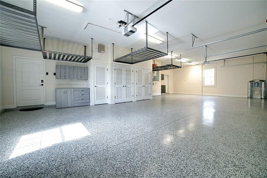 A spacious, well-lit garage features a speckled epoxy floor, overhead storage racks, and built-in cabinetry — 1792 LAKE MIONA DRIVE, THE VILLAGES, FL