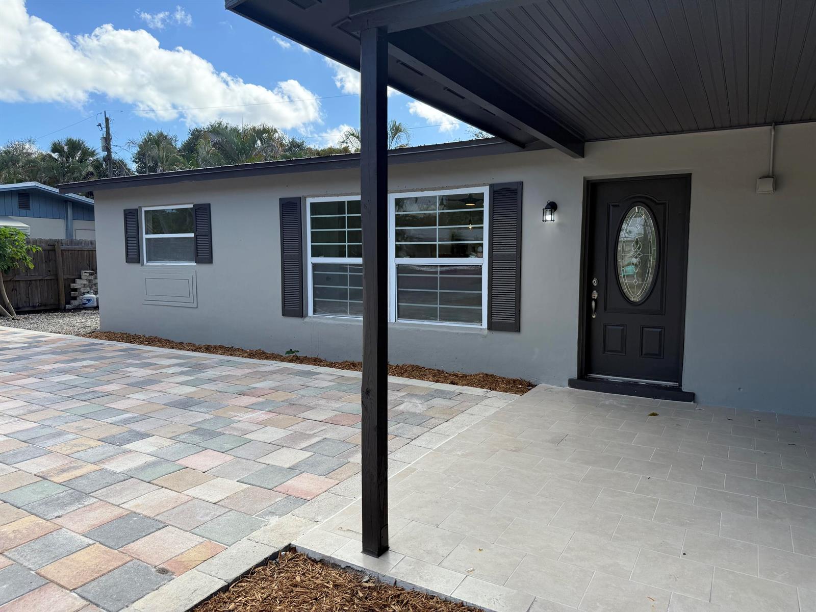 A gray house exterior features a paved patio, a dark front door, and shuttered windows — 507 SW North River Point Drive, Stuart FL 34994, STUART, FL