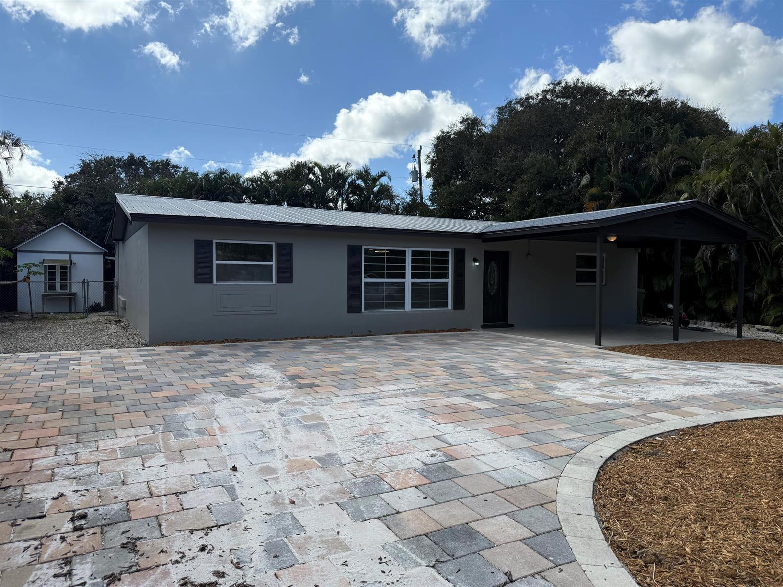 A gray single-story house features a metal roof, a paved driveway, and an attached carport — 507 SW North River Point Drive, Stuart FL 34994, STUART, FL