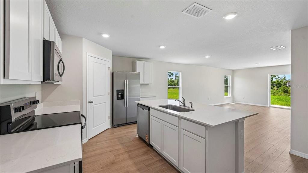 A modern kitchen with white cabinets, stainless steel appliances, and an island overlooks an open space — 12411 HOPSCOTCH AVENUE E, PALMETTO, FL