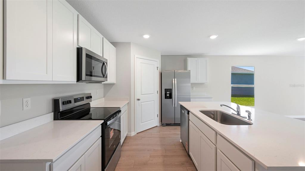 A modern kitchen features white cabinets, stainless steel appliances, and a central island with sink — 12411 HOPSCOTCH AVENUE E, PALMETTO, FL