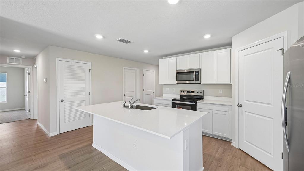 A kitchen features white cabinets, a central island with a sink, and stainless steel appliances — 12411 HOPSCOTCH AVENUE E, PALMETTO, FL