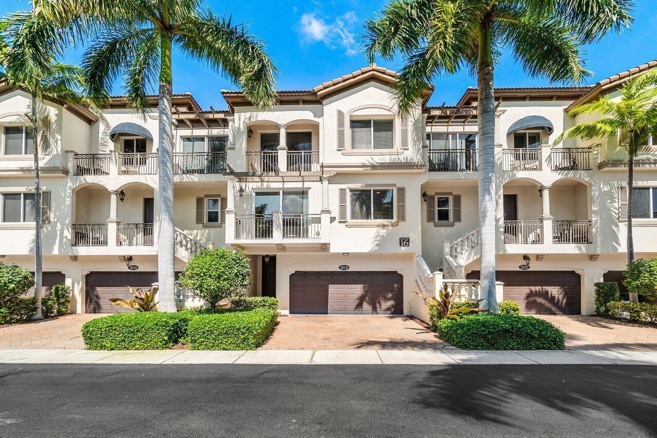 A three-story townhouse exterior features a beige stucco facade, arched balconies, and three garage doors — 3018 Waterside Circle, Boynton Beach FL 33435, BOYNTON BEACH, FL