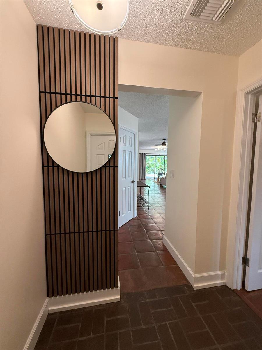 A hallway features a vertical wood-slat wall panel with a round mirror and tiled floors — 801 NE 2nd Avenue, Delray Beach FL 33444, DELRAY BEACH, FL