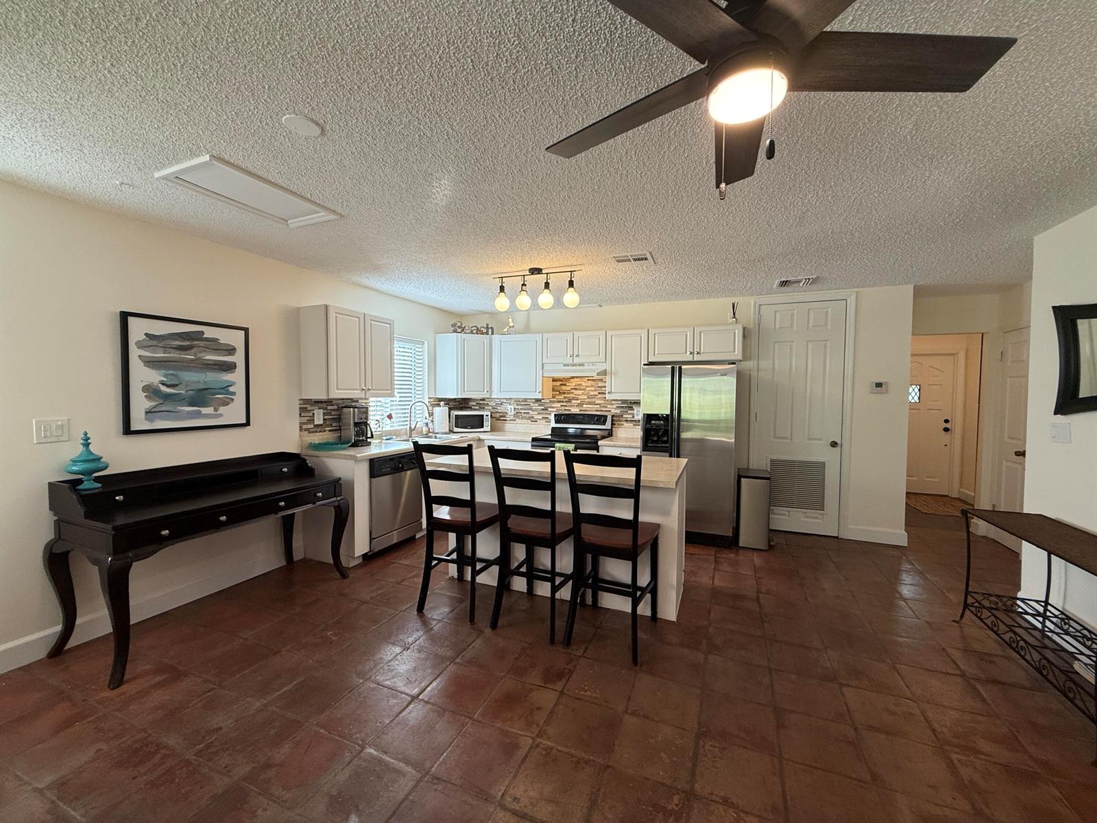 A kitchen features white cabinets, a central island with three chairs, and terracotta tile flooring — 801 NE 2nd Avenue, Delray Beach FL 33444, DELRAY BEACH, FL
