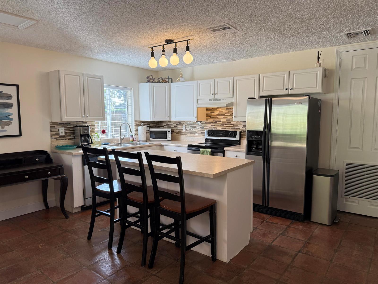 A kitchen features white cabinets, stainless steel appliances, a center island with seating, and tile flooring — 801 NE 2nd Avenue, Delray Beach FL 33444, DELRAY BEACH, FL