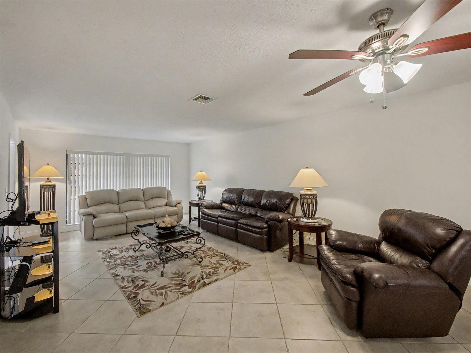 A living room features tile flooring, a ceiling fan, and three leather sofas — 4759 Storkwood Terrace # A, Boynton Beach FL 33436, BOYNTON BEACH, FL