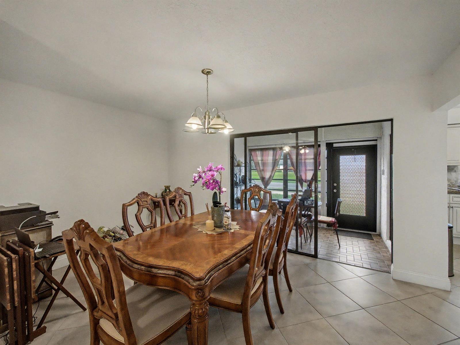 A dining room with a wooden table, six chairs, and a sliding glass door entrance — 4759 Storkwood Terrace # A, Boynton Beach FL 33436, BOYNTON BEACH, FL