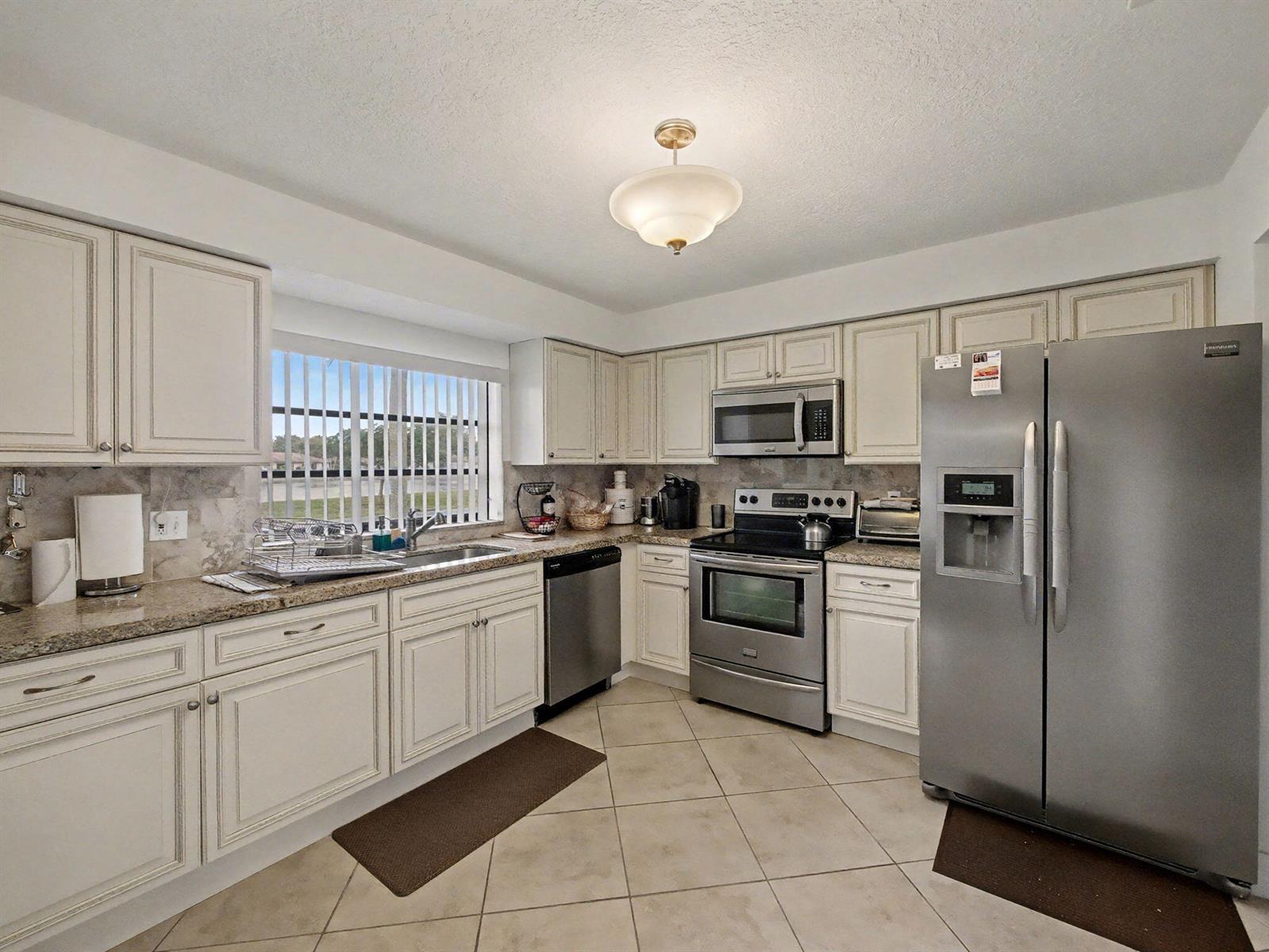 A kitchen with off-white cabinets, granite countertops, stainless steel appliances, and tile flooring — 4759 Storkwood Terrace # A, Boynton Beach FL 33436, BOYNTON BEACH, FL
