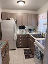 A kitchen with wood-tone cabinets, a white refrigerator, a double sink, and tiled flooring — 5906 17TH STREET W UNIT C35, BRADENTON, FL