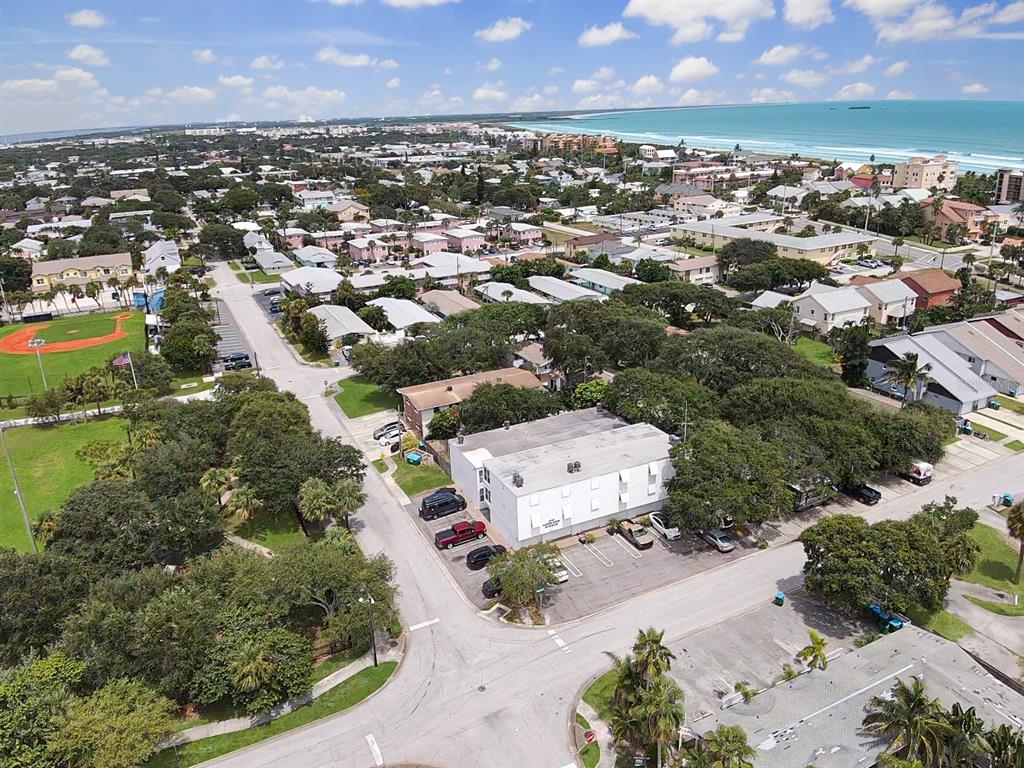 An aerial view shows a white commercial building surrounded by trees, parking, and nearby houses — 404 HARRISON AVENUE, CAPE CANAVERAL, FL