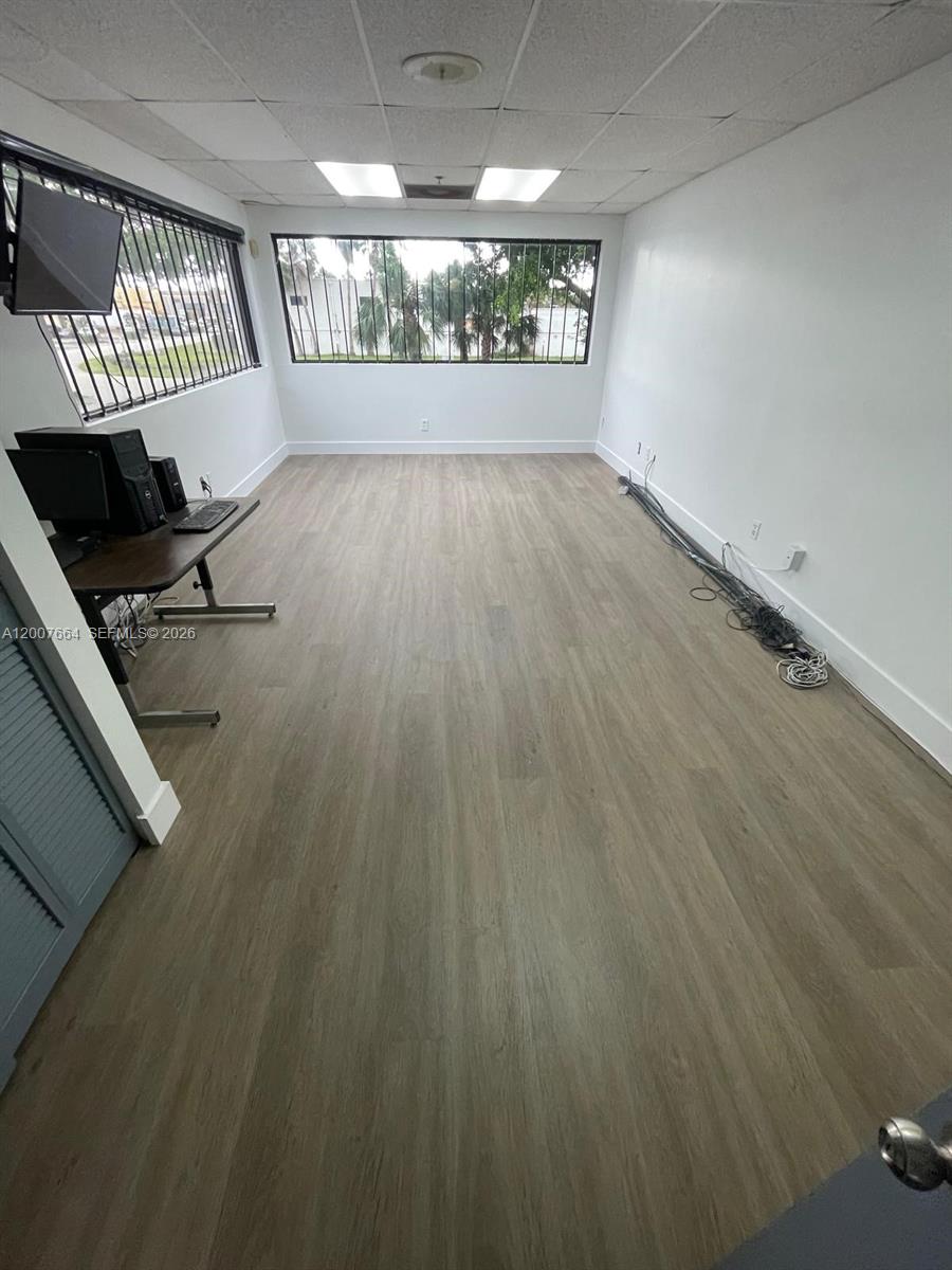 An office room features wood-look flooring, white walls, a desk, and windows with security bars — 9387 NW 13th St # 7, Doral FL 33172, DORAL, FL