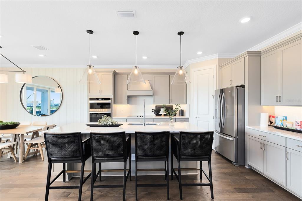 A modern kitchen features a large island with four black chairs and stainless steel appliances — 2216 BRANCHED OAK ROAD, ST CLOUD, FL