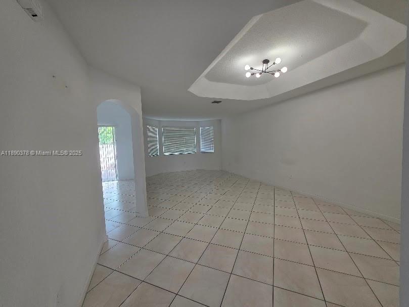 An empty room with white walls, tiled floors, and a tray ceiling with a chandelier — 11525 NW 71st St # 11525, Doral FL 33178, DORAL, FL
