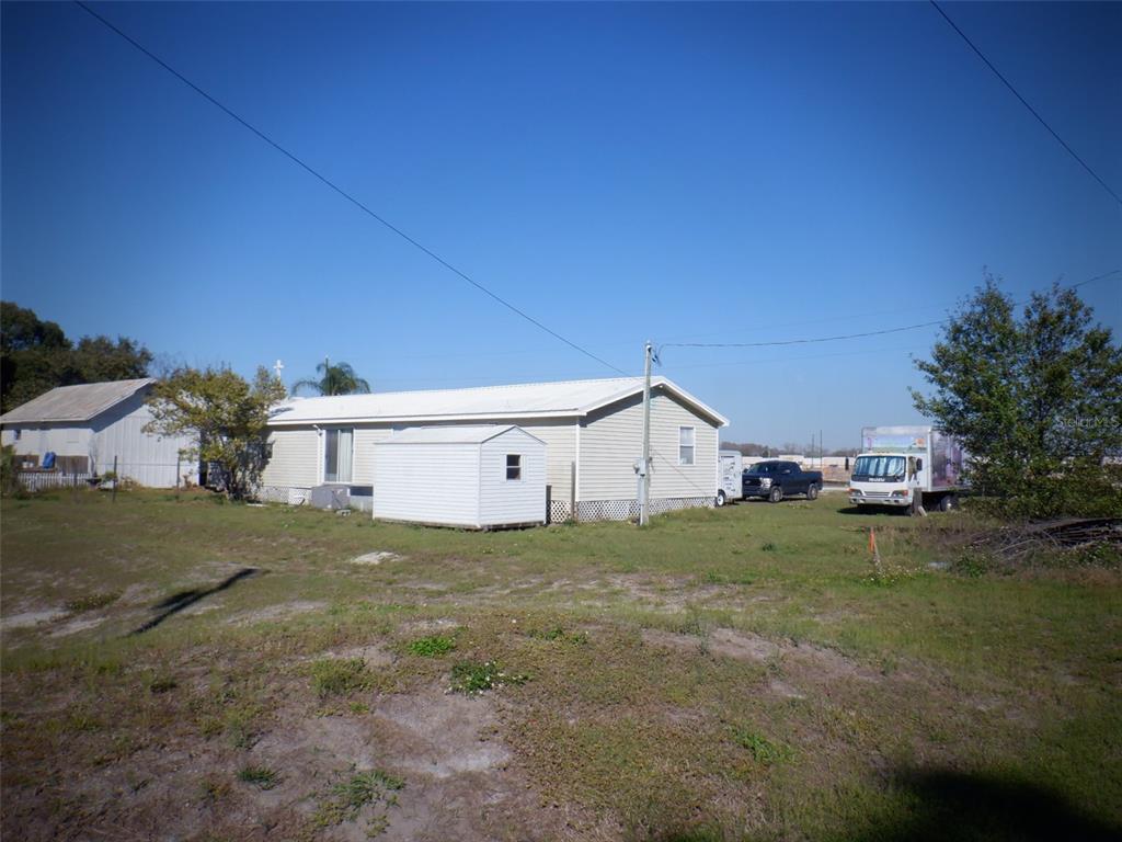 A light-colored manufactured home sits on a grassy lot with a small shed nearby — 2239 OLD GUNN HIGHWAY, ODESSA, FL