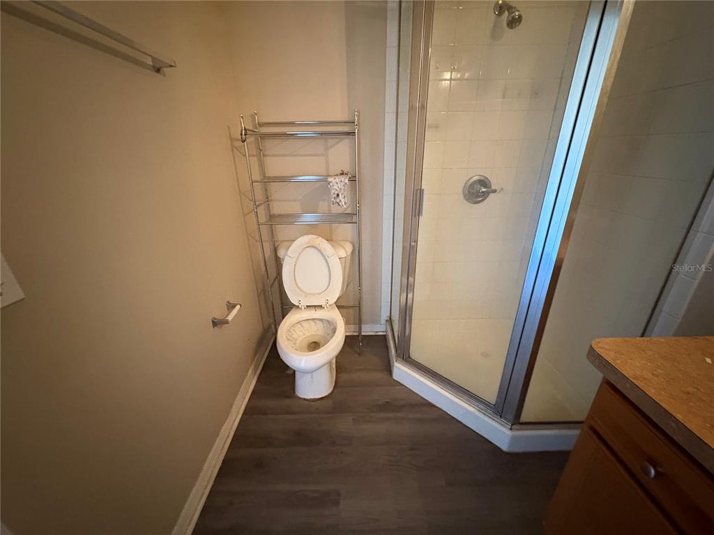 A bathroom features a toilet with a metal storage rack, a corner shower, and wood-look flooring — 13912 SW 61ST CIRCLE, OCALA, FL