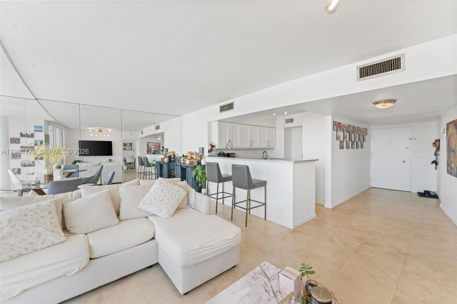 A living room with a white sectional sofa, breakfast bar, and mirrored wall — 900 Bay Dr # 421, Miami Beach FL 33141, MIAMI BEACH, FL