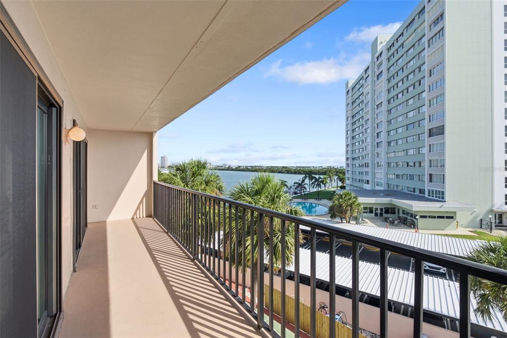 A balcony with a metal railing overlooks a swimming pool, palm trees, and a large building — 51 ISLAND WAY UNIT 411, CLEARWATER BEACH, FL