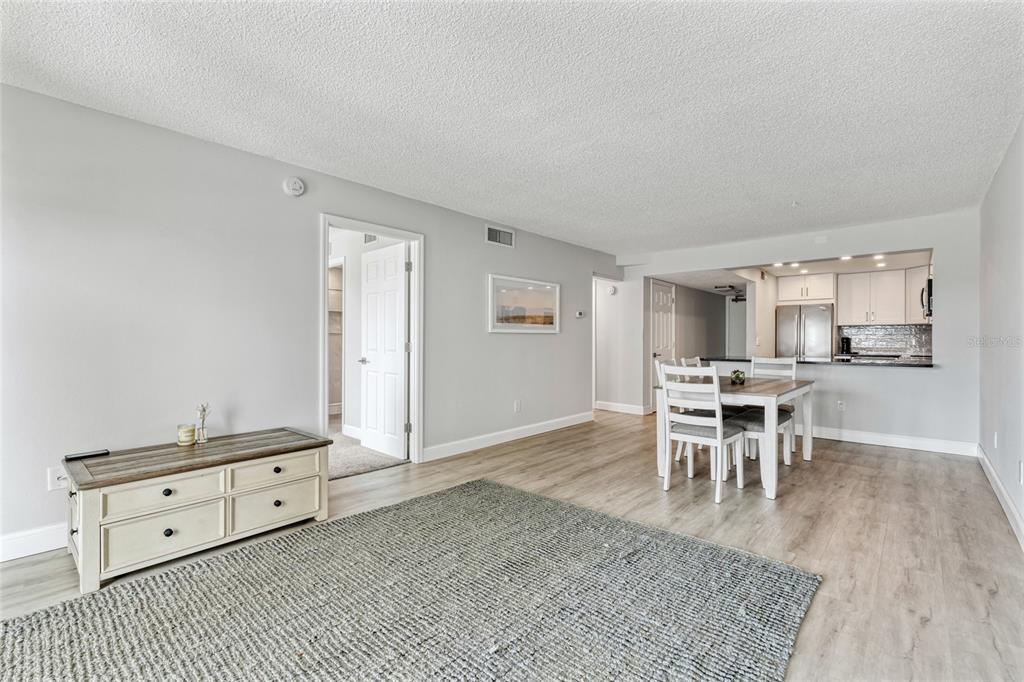 A living room with light wood flooring, a gray area rug, and an adjacent dining area — 51 ISLAND WAY UNIT 411, CLEARWATER BEACH, FL