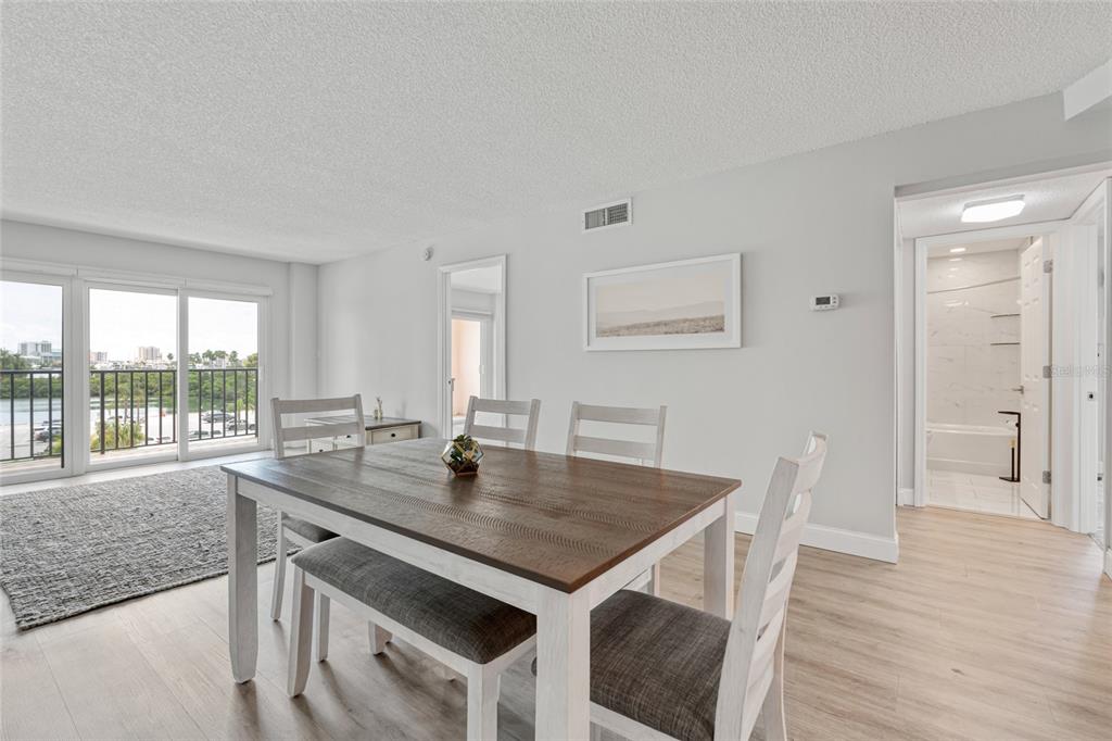 A dining area with a wooden table and chairs overlooks a balcony with water views — 51 ISLAND WAY UNIT 411, CLEARWATER BEACH, FL