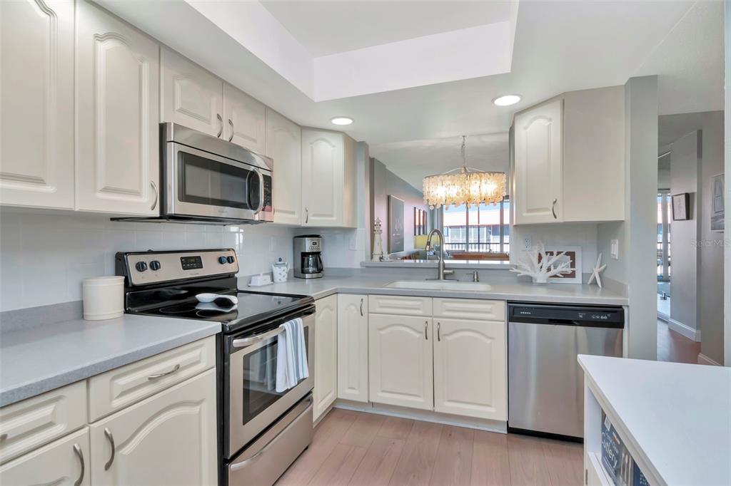 A kitchen features white cabinets, stainless steel appliances, and a pass-through window to the dining area — 17580 GULF BOULEVARD UNIT 403, REDINGTON SHORES, FL