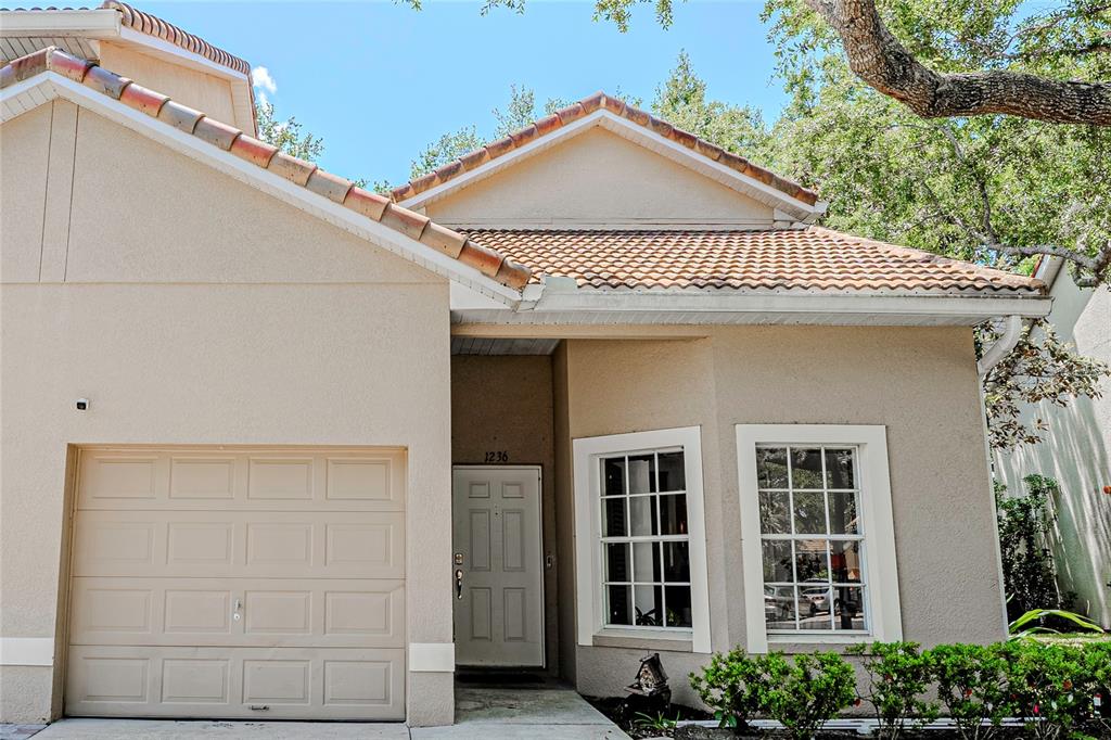 A tan stucco house features a single-car garage, a tiled roof, and two front windows — 1236 N FAIRWAY DRIVE, APOPKA, FL