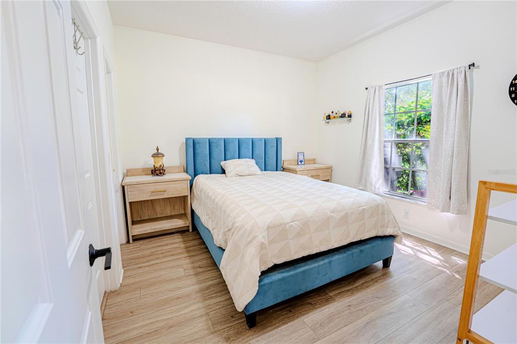 A bedroom features a blue upholstered bed, light wood nightstands, and wood-look flooring — 1236 N FAIRWAY DRIVE, APOPKA, FL