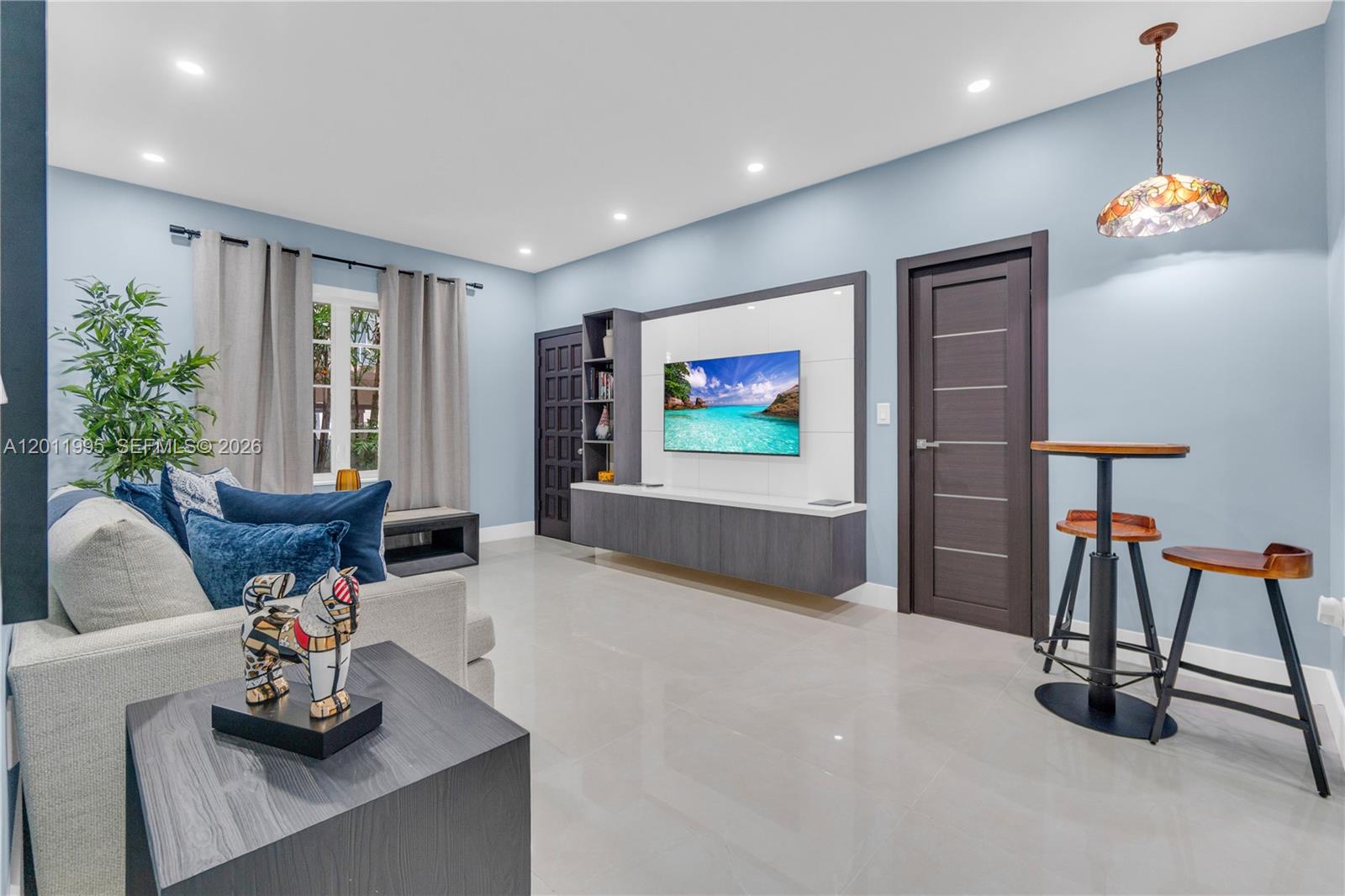 A living room features light blue walls, a wall-mounted television, and a high-top table — 1569 Euclid Ave # 7, Miami Beach FL 33139, MIAMI BEACH, FL