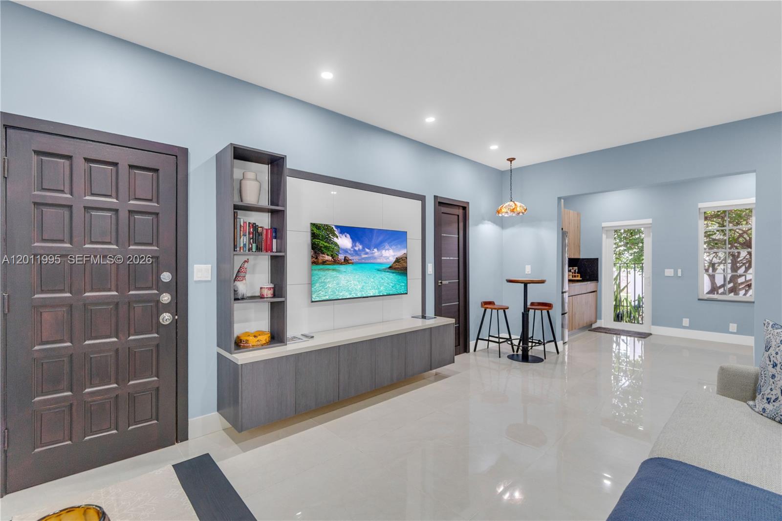A living room features light blue walls, a wall-mounted television unit, and tile flooring — 1569 Euclid Ave # 7, Miami Beach FL 33139, MIAMI BEACH, FL