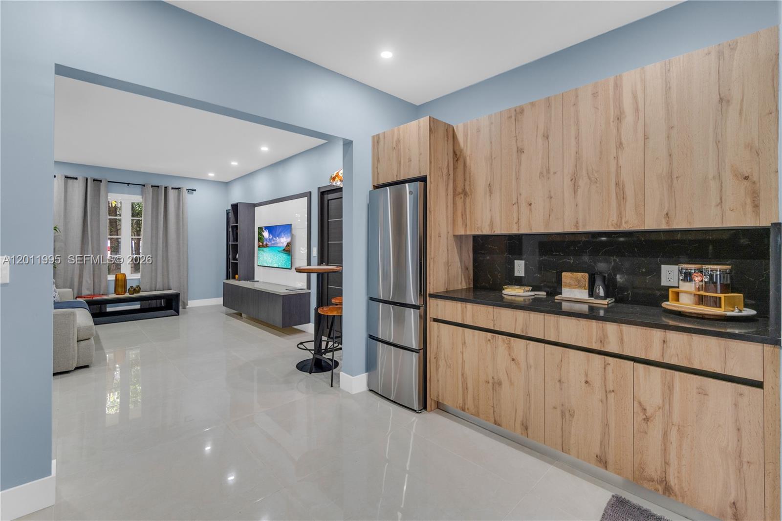A kitchen with wood-grain cabinets and black countertops opens into a living area — 1569 Euclid Ave # 7, Miami Beach FL 33139, MIAMI BEACH, FL