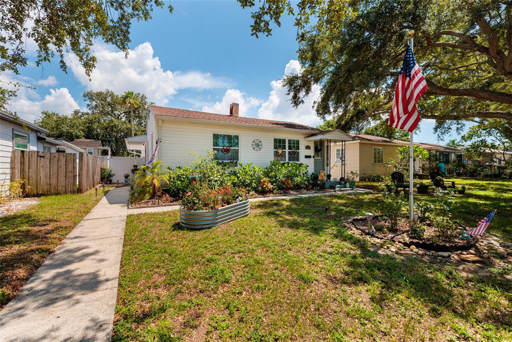 A single-story house with white siding, a front garden, and an American flag on a pole — 1220 56TH AVENUE N, ST PETERSBURG, FL
