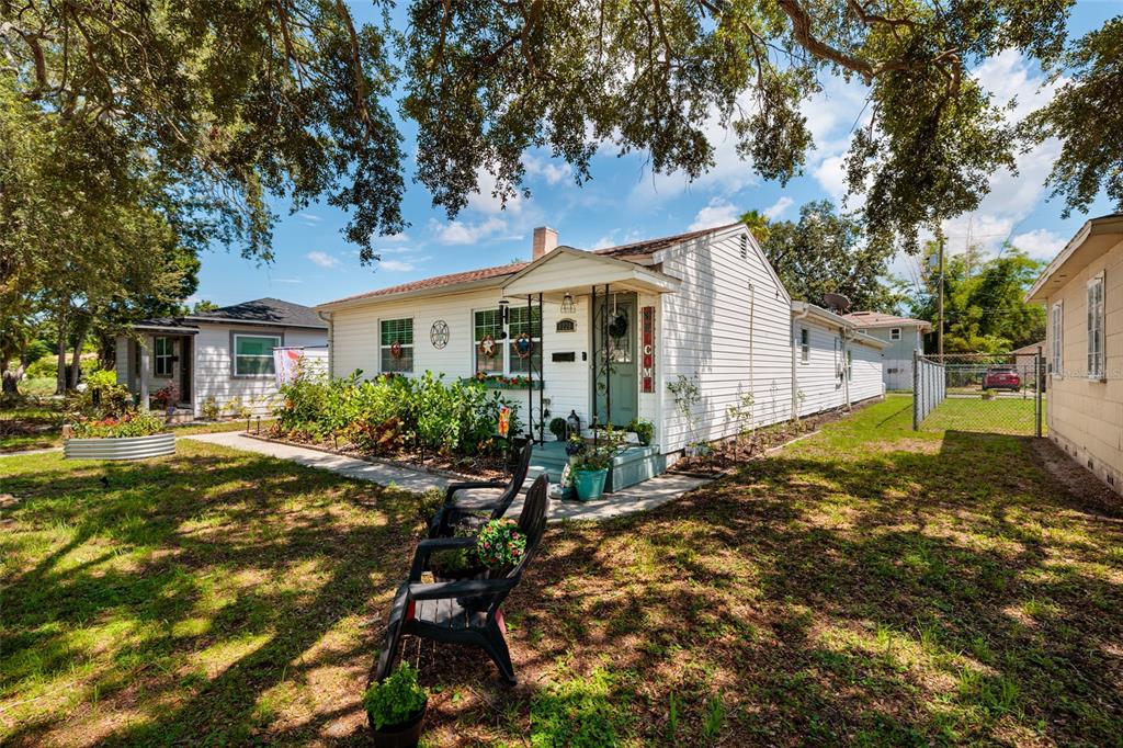 A white single-story house with a front porch, lawn, and two chairs in the yard — 1220 56TH AVENUE N, ST PETERSBURG, FL