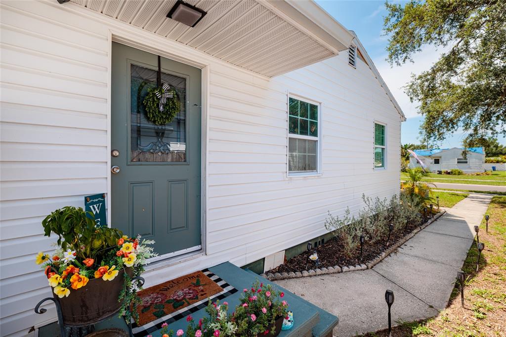 A white-sided house features a teal front door, a small porch, and a concrete walkway — 1220 56TH AVENUE N, ST PETERSBURG, FL