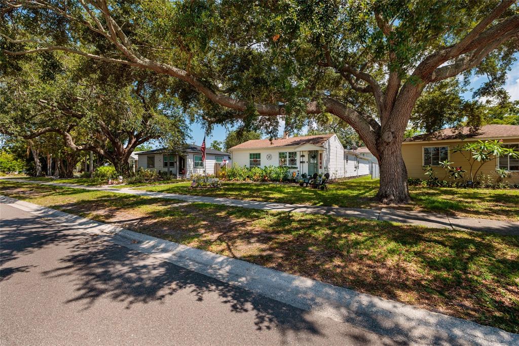 A street view of three single-story houses shaded by large oak trees along a sidewalk — 1220 56TH AVENUE N, ST PETERSBURG, FL