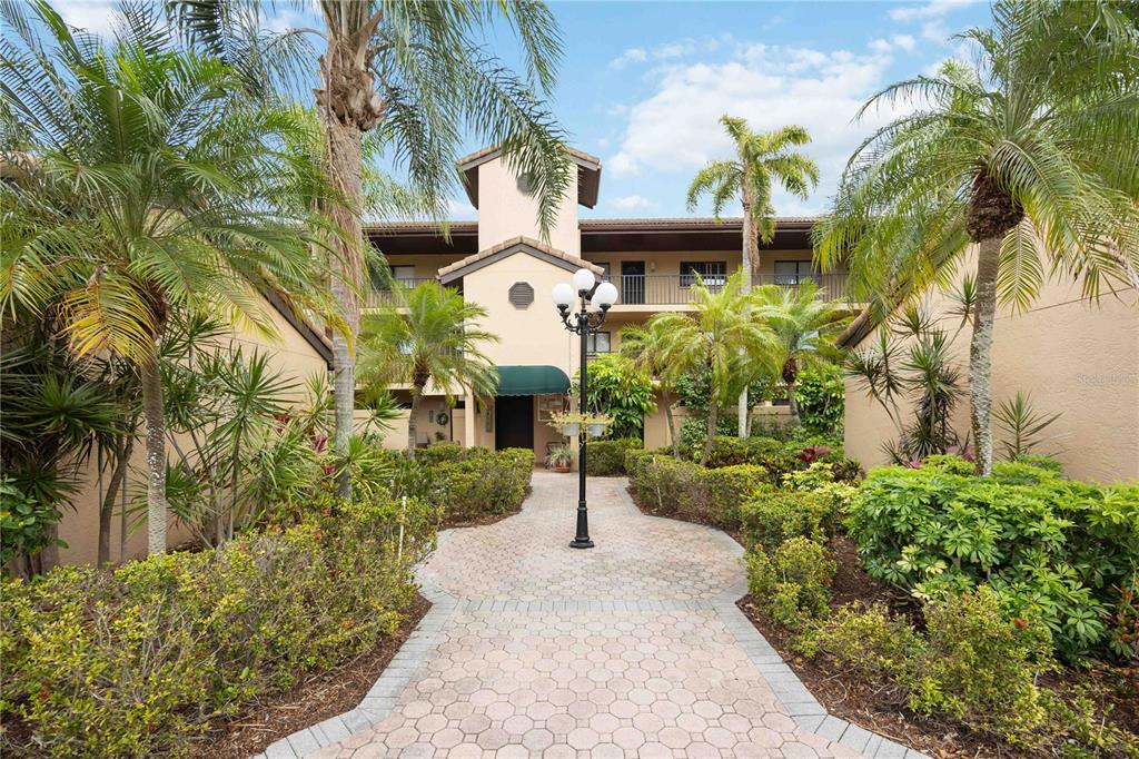 A paved walkway leads to the entrance of a multi-story apartment building with palm trees — 5627 ASHTON WAY UNIT 5627, SARASOTA, FL