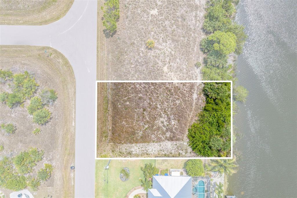 An aerial view shows a rectangular vacant lot bordered by a road and a lake — 15424 HENNIPEN CIRCLE, PORT CHARLOTTE, FL