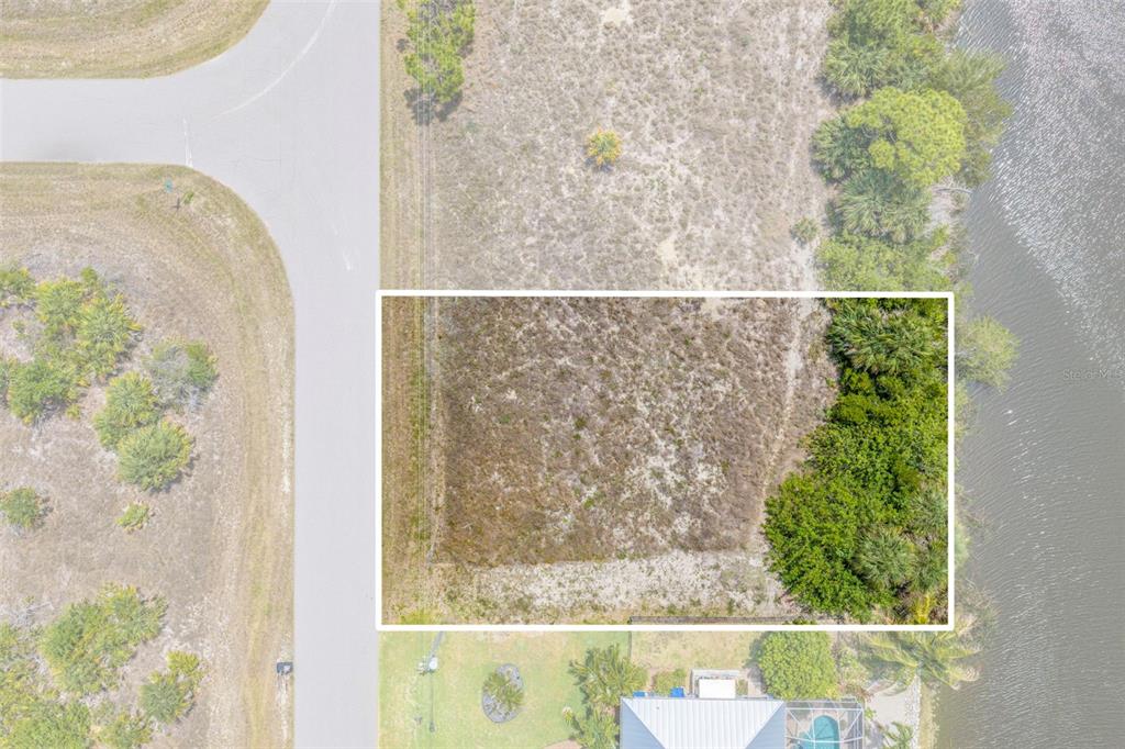 An aerial view shows a rectangular vacant lot bordered by a road, vegetation, and water — 15424 HENNIPEN CIRCLE, PORT CHARLOTTE, FL