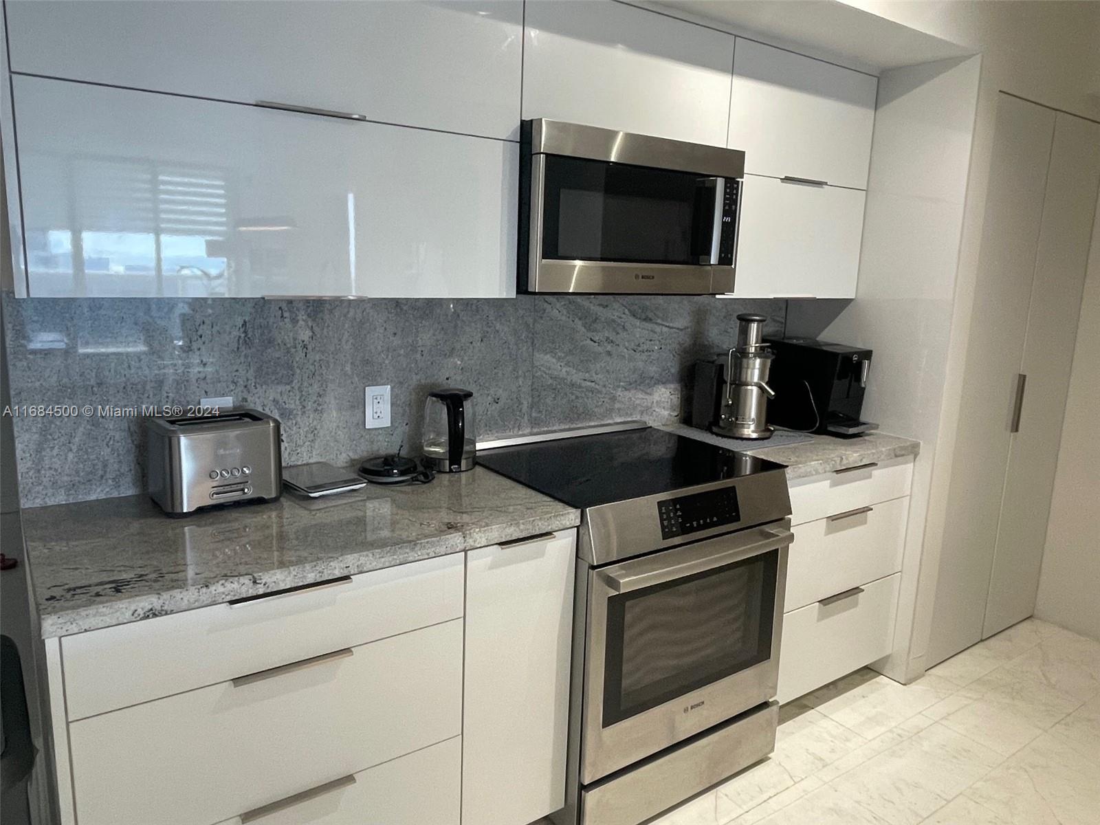 A modern kitchen features white cabinets, stainless steel appliances, and a gray granite backsplash — 1830 S Ocean Dr # 2604, Hallandale Beach FL 33009, HALLANDALE BEACH, FL