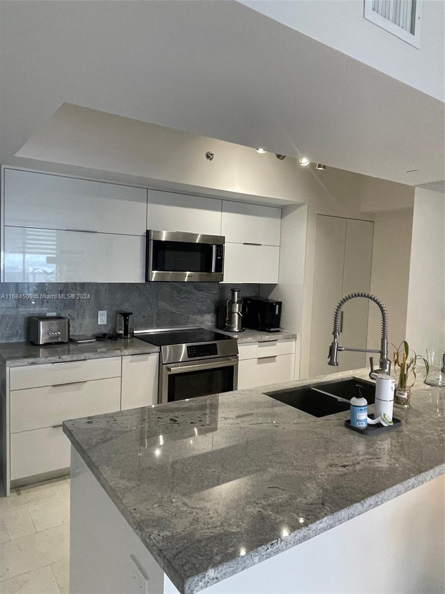 A modern kitchen features white cabinetry, granite countertops, stainless steel appliances, and a central island — 1830 S Ocean Dr # 2604, Hallandale Beach FL 33009, HALLANDALE BEACH, FL