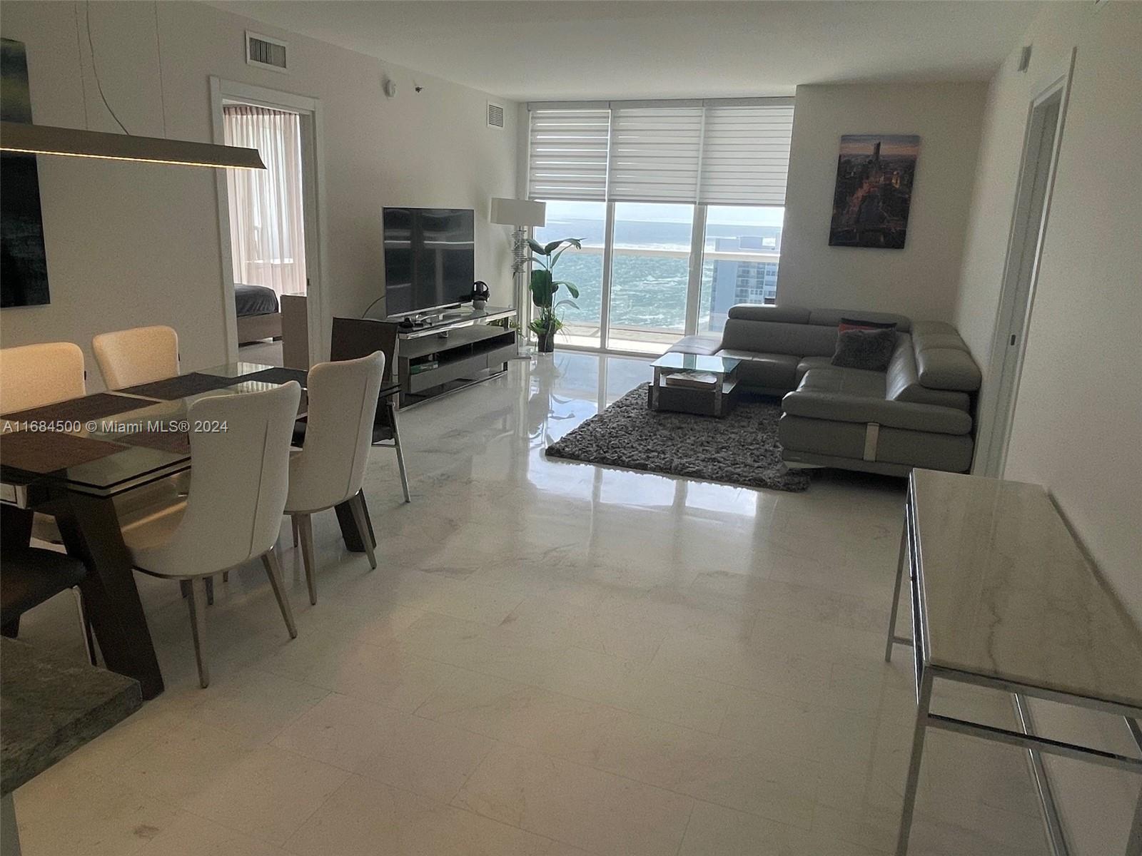 A modern living and dining area features marble floors, a grey sectional, and ocean views — 1830 S Ocean Dr # 2604, Hallandale Beach FL 33009, HALLANDALE BEACH, FL