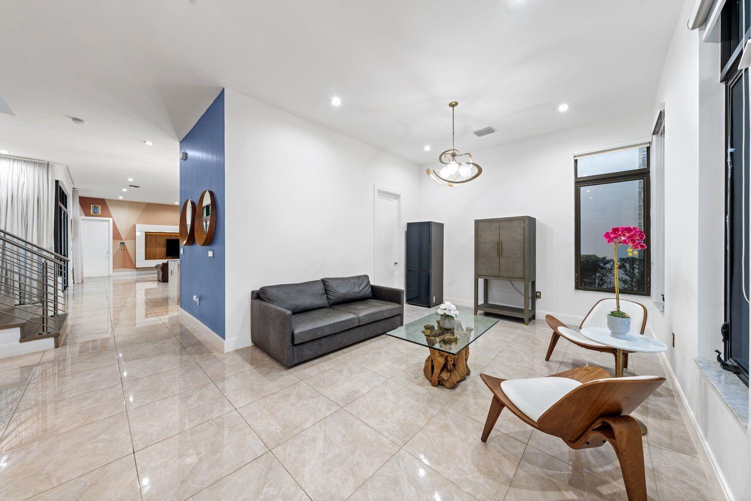 A modern living room features a grey sofa, glass coffee table, and two wooden chairs — 8225 Central Park Boulevard, Doral FL 33166, DORAL, FL