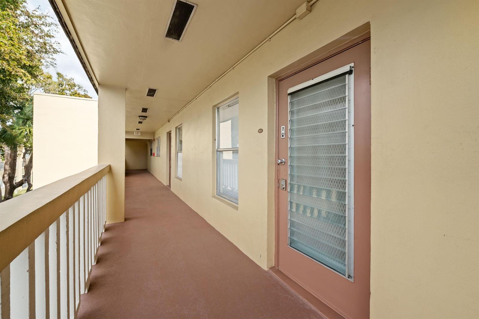 An outdoor apartment hallway with a brown door, windows, and a white railing — 6000 NW 64th Avenue # 303, Tamarac FL 33319, TAMARAC, FL